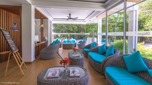 Un moderno vestíbulo de hotel con muebles de mimbre, un mostrador de recepción y amplias ventanas que ofrecen vistas al exterior.