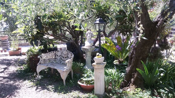 Un jardín con un banco blanco, un farol de piedra y varias plantas en macetas.