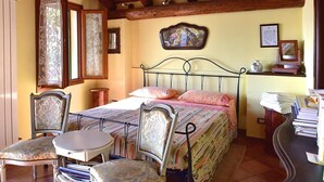 Un dormitorio con una cama, dos sillas, una mesita y un escritorio con libros y papeles.