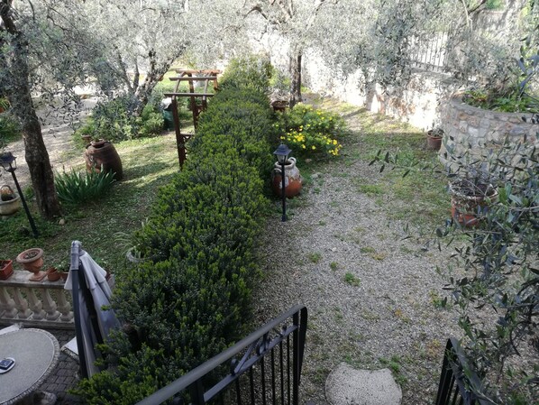 Un jardín con un sendero de grava, plantas en macetas, un banco de madera y un muro de piedra.