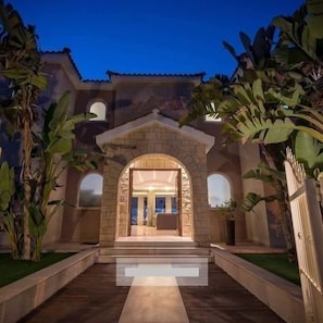 A building with a stone entrance, a central archway, and a paved pathway leading to the entrance. - villa kristia (Paphos)