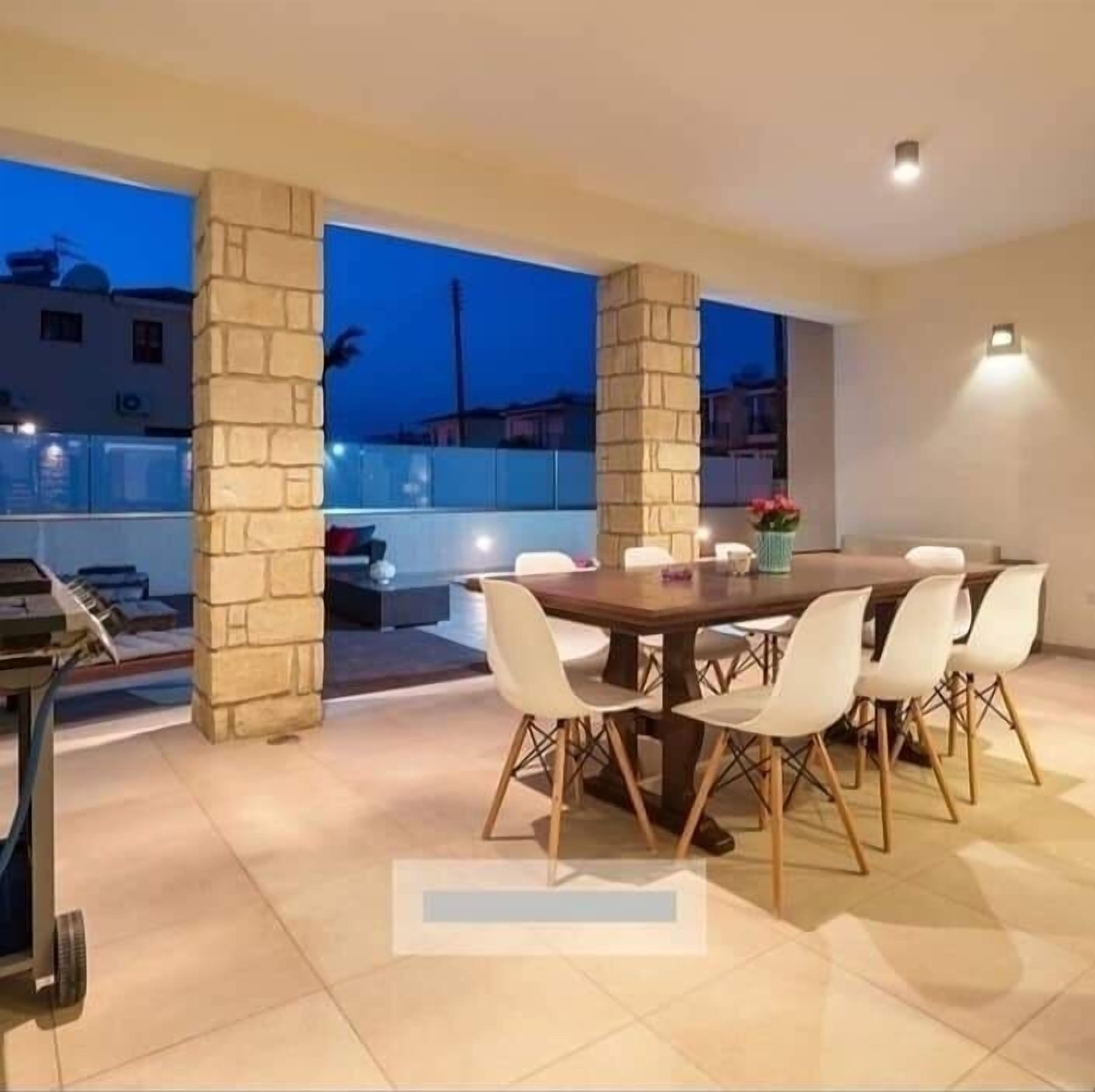 An outdoor dining area with a stone column structure, a round table, and white chairs.