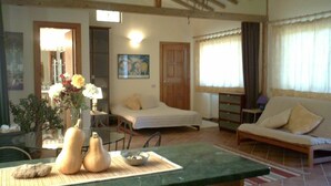 A cozy room with a bed, a sofa, a dining table with a bowl and two gourds, and a painting on the wall.