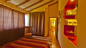 A room with a large bed, a chair, a red accent wall, and a hallway leading to another room.