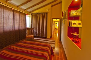 A room with a large bed, a chair, a red accent wall, and a hallway leading to another room.