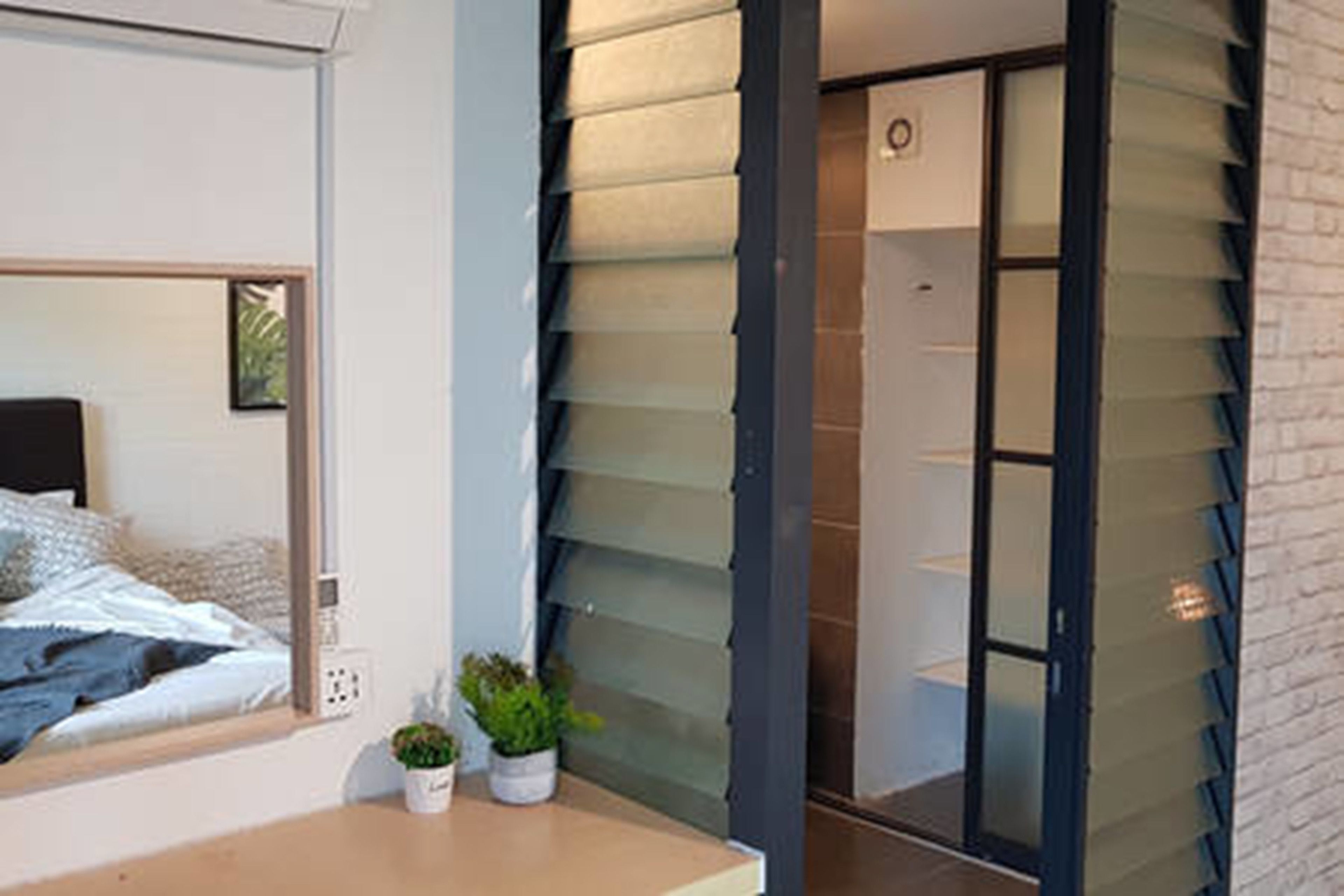 A modern bedroom with a bed, bedside plants, and a large window.