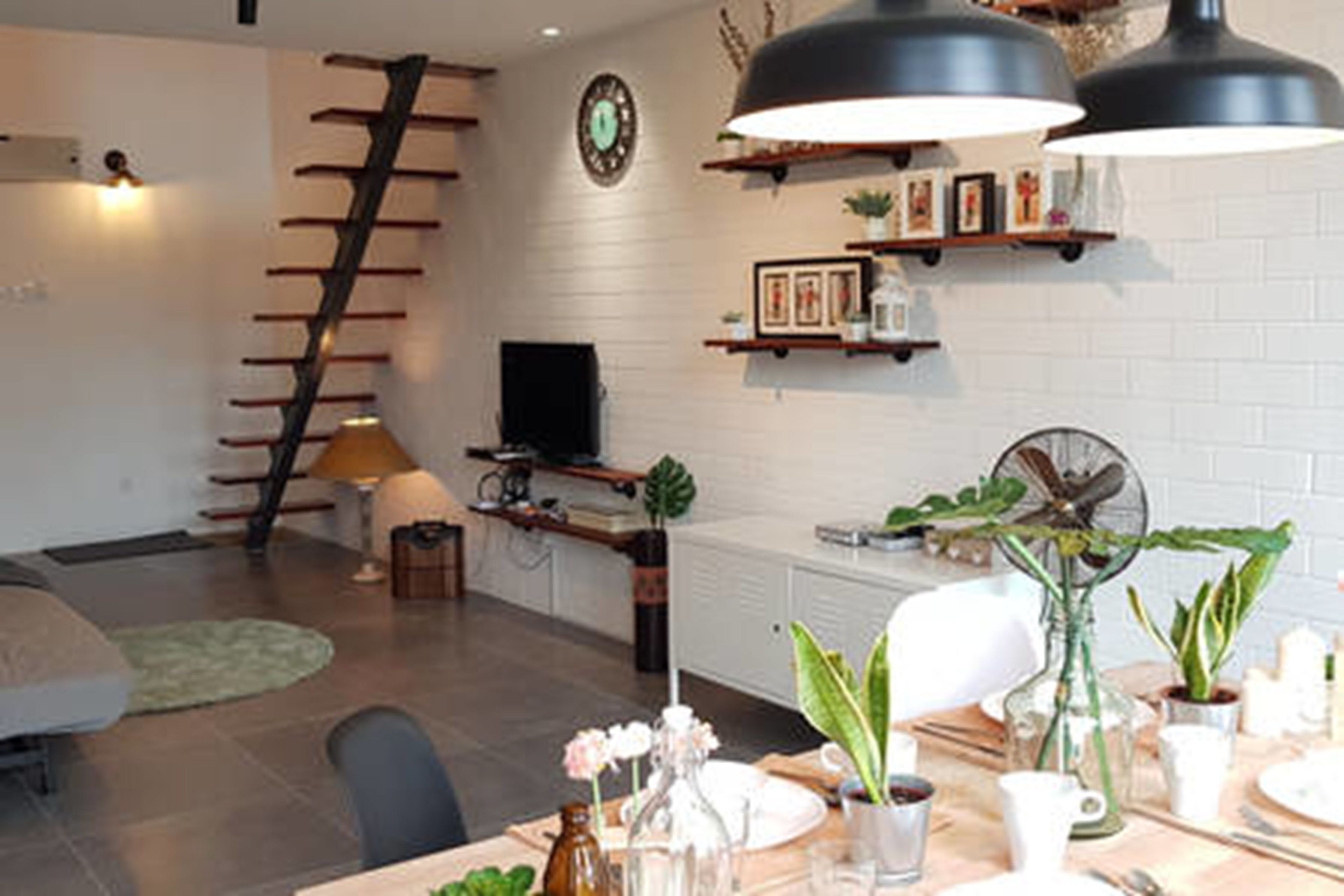 A modern living room with a staircase, a dining area with a table set for two, and a kitchen in the background.