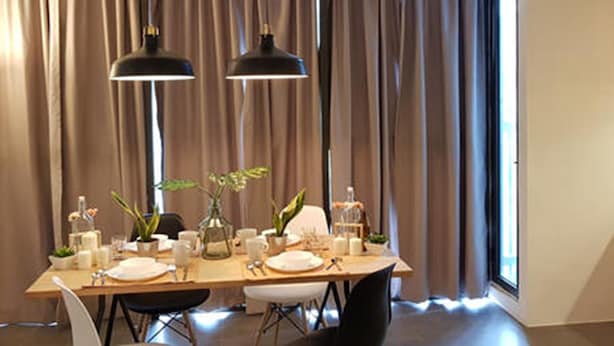 A dining area with a table set for four, two pendant lights, and a view through large windows with curtains. - Duplex Loft Empire Damansara (Petaling Jaya)