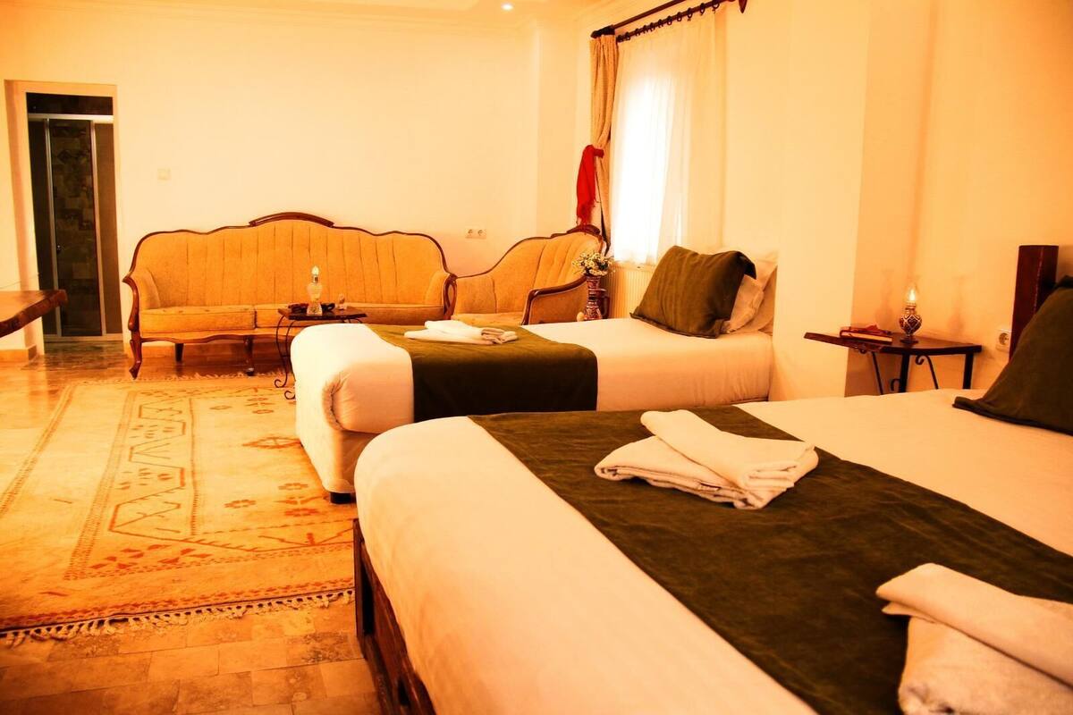 A hotel room with two beds, a sofa, a small table, and a lamp.