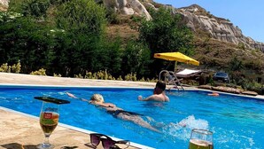A pool area with clear blue water, surrounded by rocky terrain and greenery. - Kufe Hotel (Nevsehir)