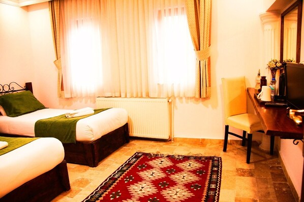 A hotel room with two beds, a desk, a chair, a radiator, and a window with curtains. - Kufe Hotel (Nevsehir)