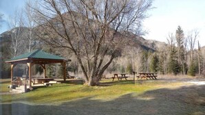Un quiosco con mesas de picnic en un parque con montañas al fondo.