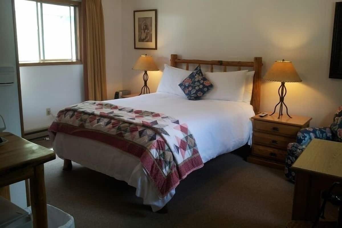 A neatly arranged hotel room with a bed, two bedside tables with lamps, a window with curtains, and a wall-mounted picture.