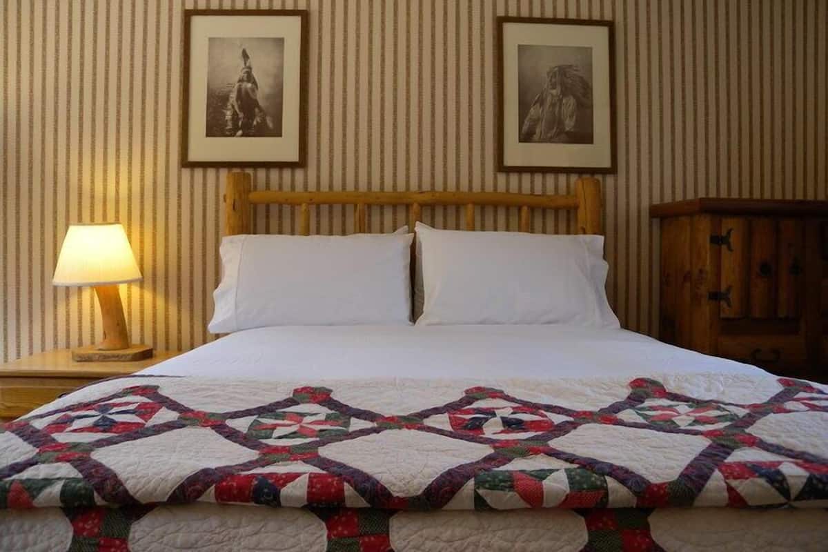 A neatly made bed with a quilt, a wooden headboard, a nightstand with a lamp, and two framed pictures on the wall.