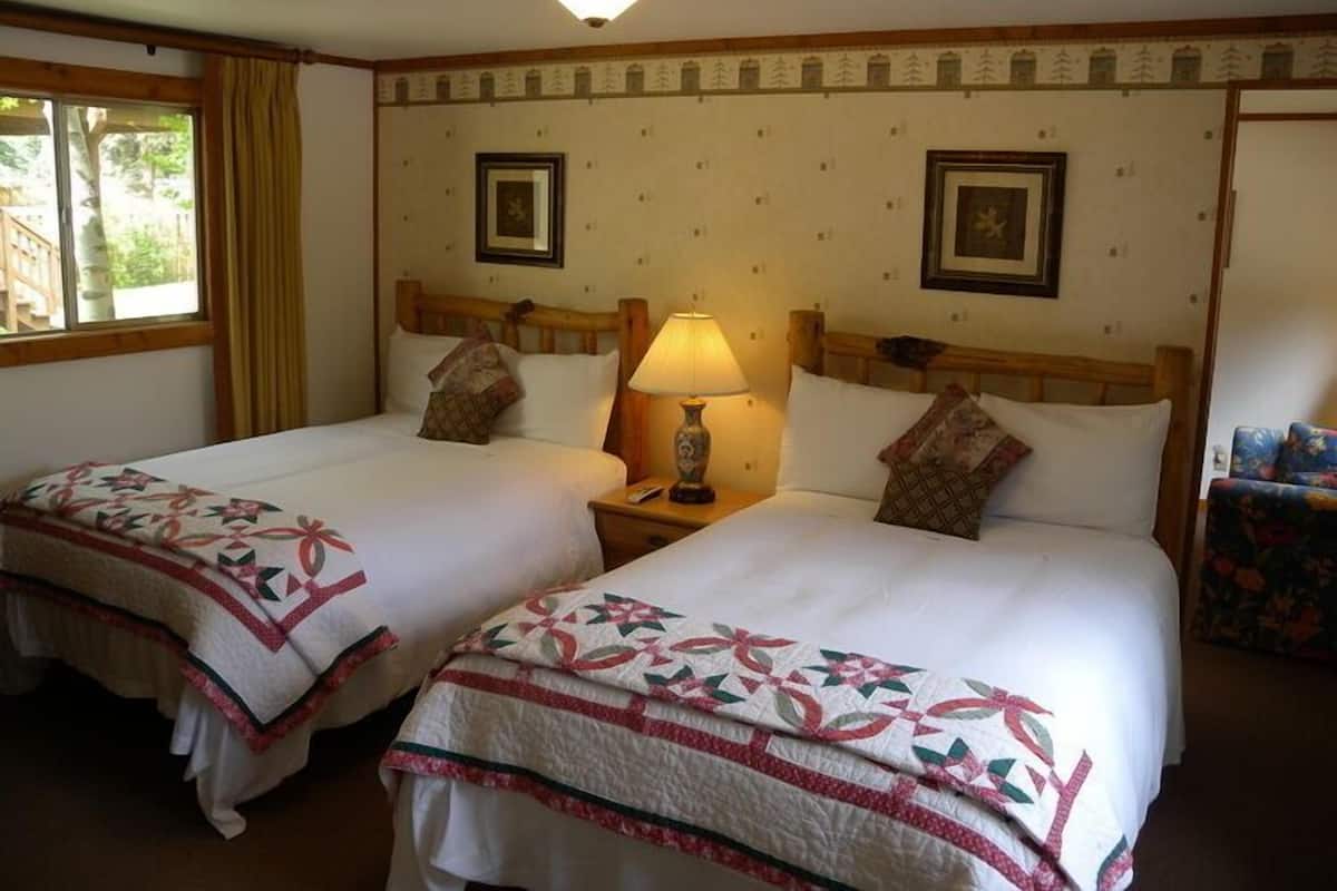 A double room with two beds, each with a floral-patterned bedspread, a bedside lamp, and framed pictures on the wall.