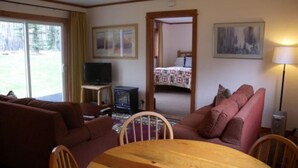 Un salón acogedor con una mesa de madera, sofás, un televisor y una cama al fondo.