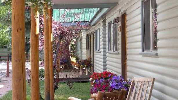 Un porche de madera con un banco, una jardinera con flores y una casa con techo verde.