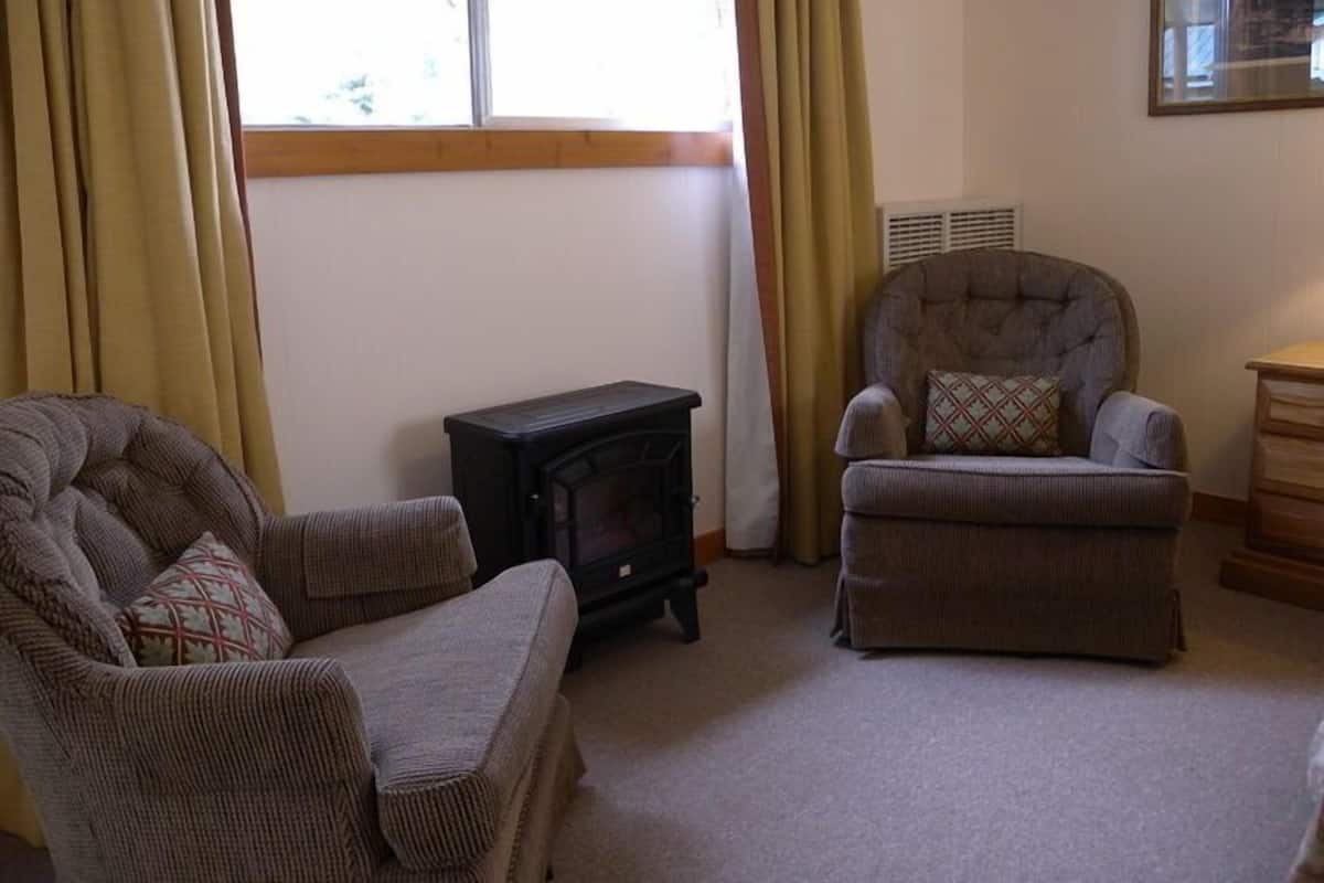 A cozy living room with a fireplace, two armchairs, and a wooden sideboard.