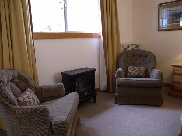Una sala de estar acogedora con chimenea, dos sillones y un aparador de madera.