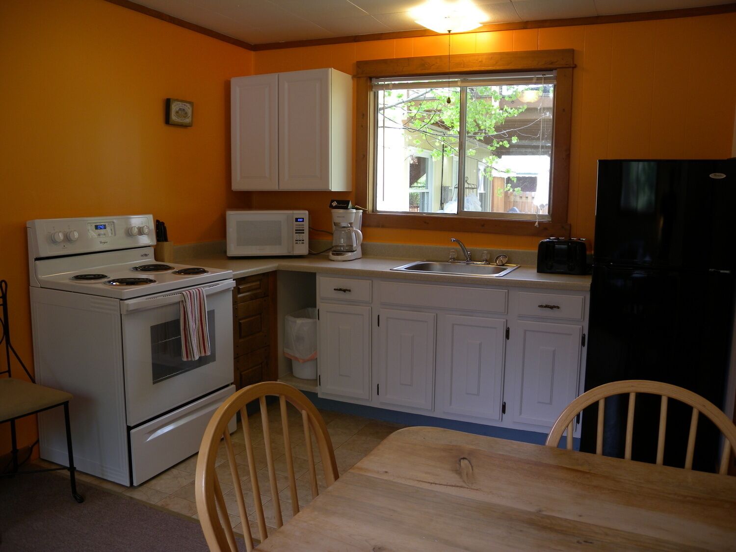 A compact kitchen with white cabinets, a stove, a microwave, a sink, and a refrigerator.