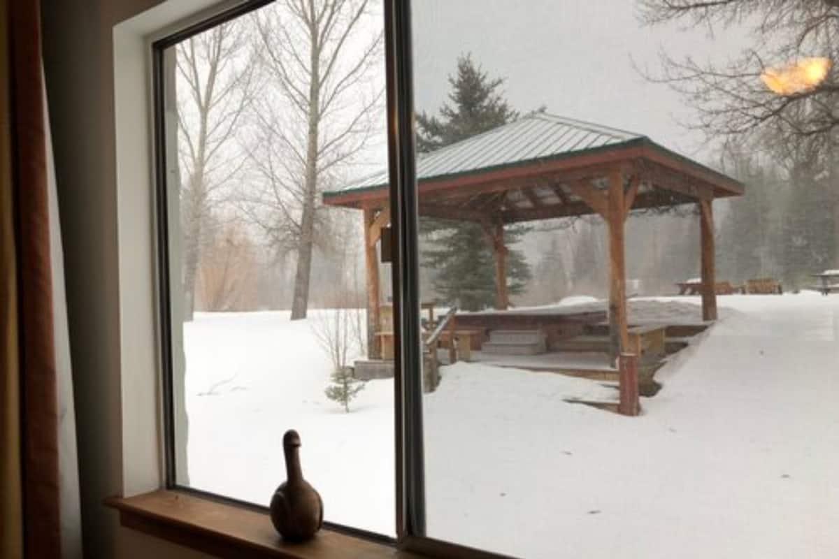 A view through a window of a wooden gazebo in a snowy outdoor area.