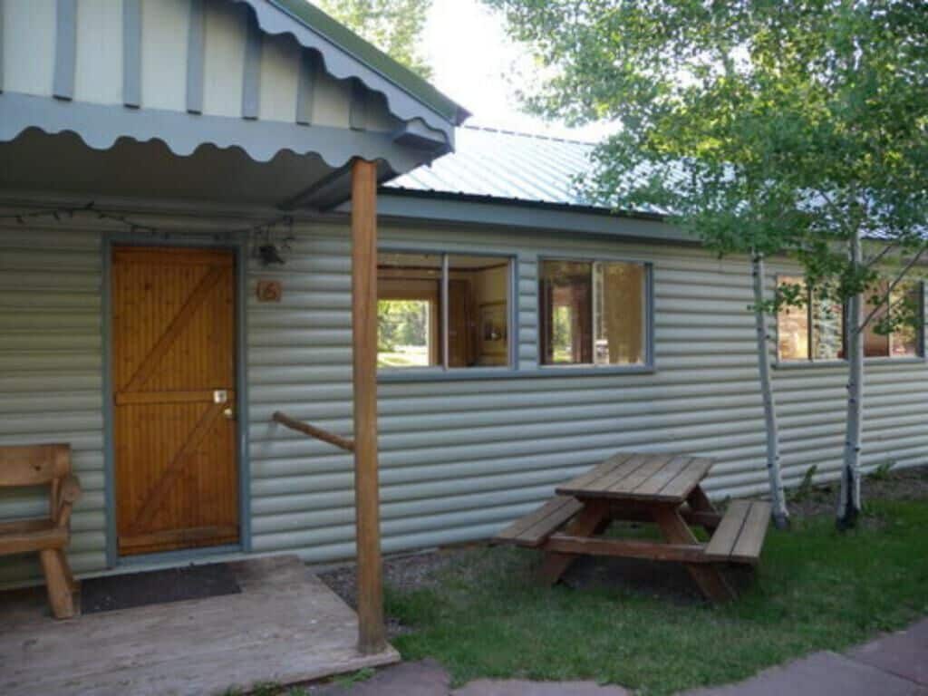 A single-story cabin with a wooden door, windows, and a picnic table in the yard.
