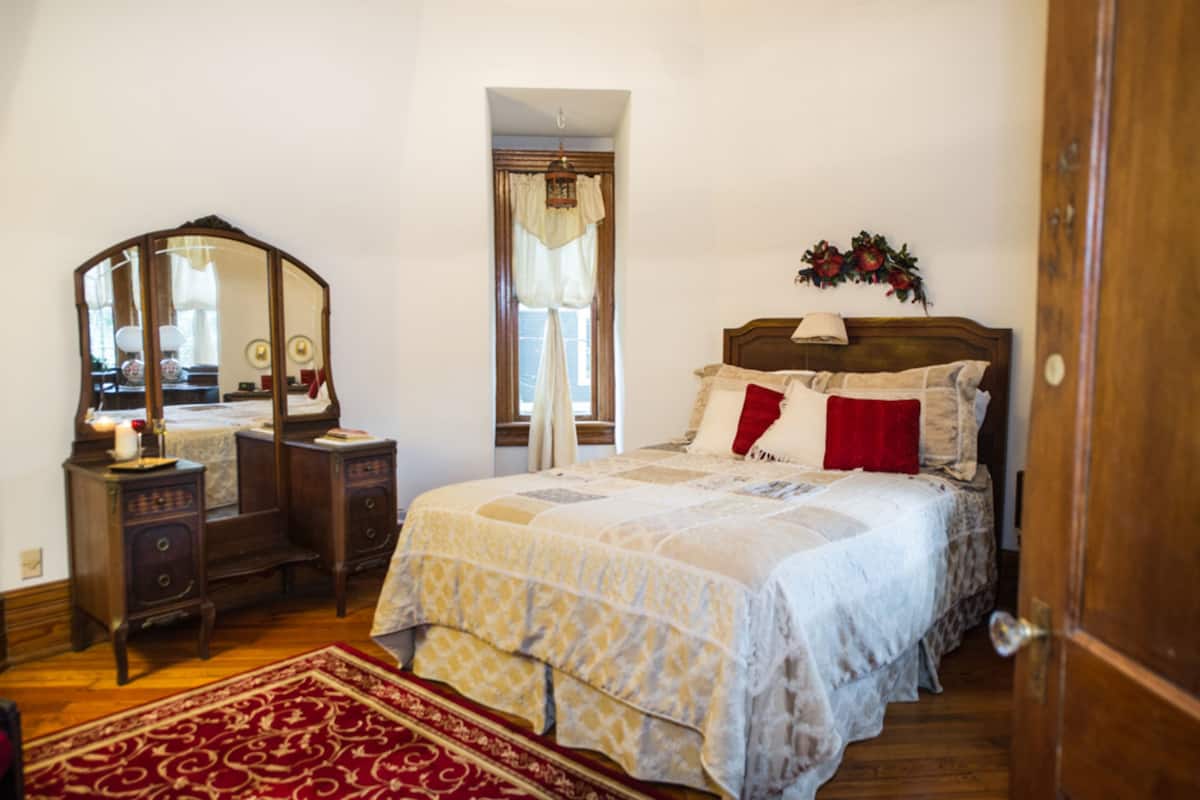 A bedroom with a wooden bed, a nightstand, a mirror, and a red and white patterned rug.