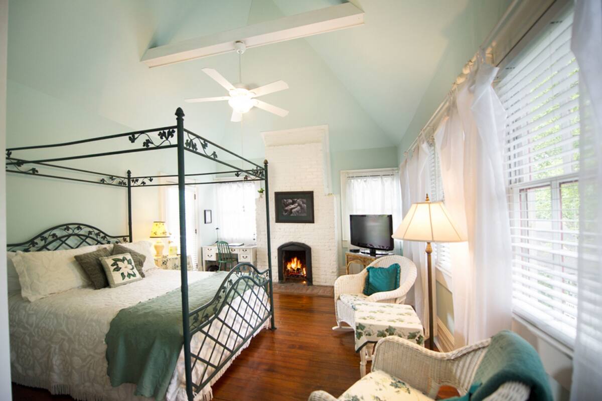 A four-poster bed with a television and a fireplace in a room with a high ceiling and a ceiling fan.