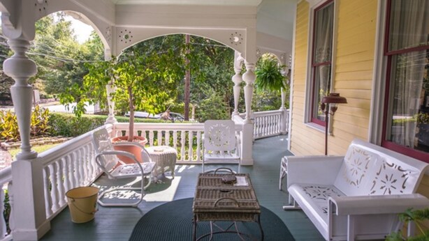 A covered porch with white railings, a white sofa, a wicker table, and a potted plant. - Sugar Magnolia Bed & Breakfast (Atlanta)