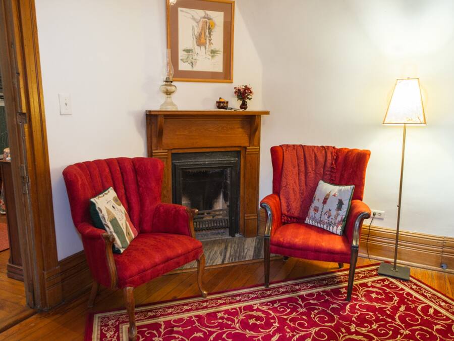 A room with two red armchairs, a fireplace, a framed picture above the mantel, and a floor lamp.