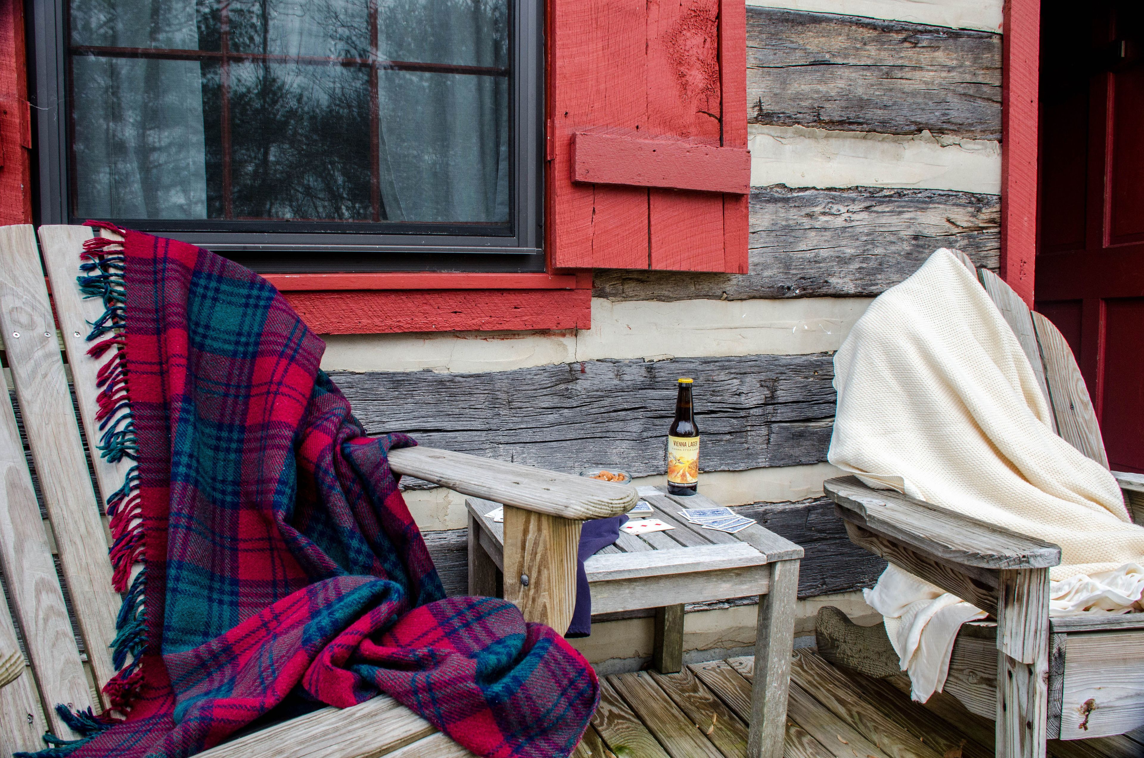 A rustic wooden bench with a plaid blanket, a bottle of beer, and a small table with a card and a bottle.