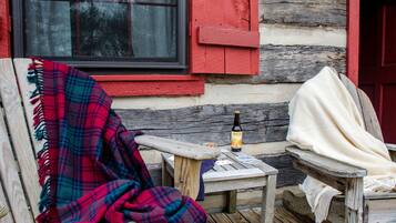 A rustic wooden bench with a plaid blanket, a bottle of beer, and a small table with a card and a bottle.
