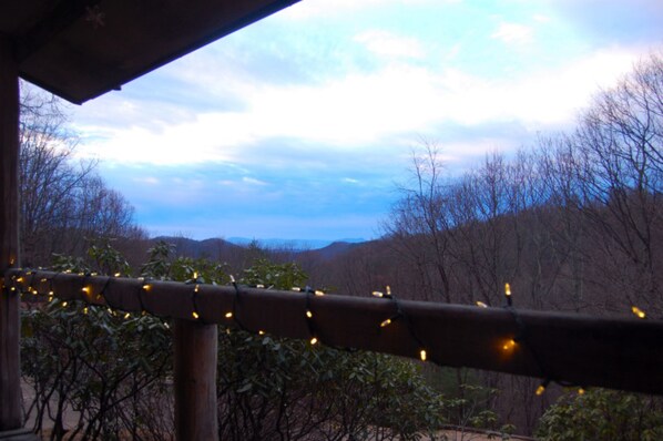 A view from a covered outdoor area with string lights, overlooking a forested landscape and distant hills.