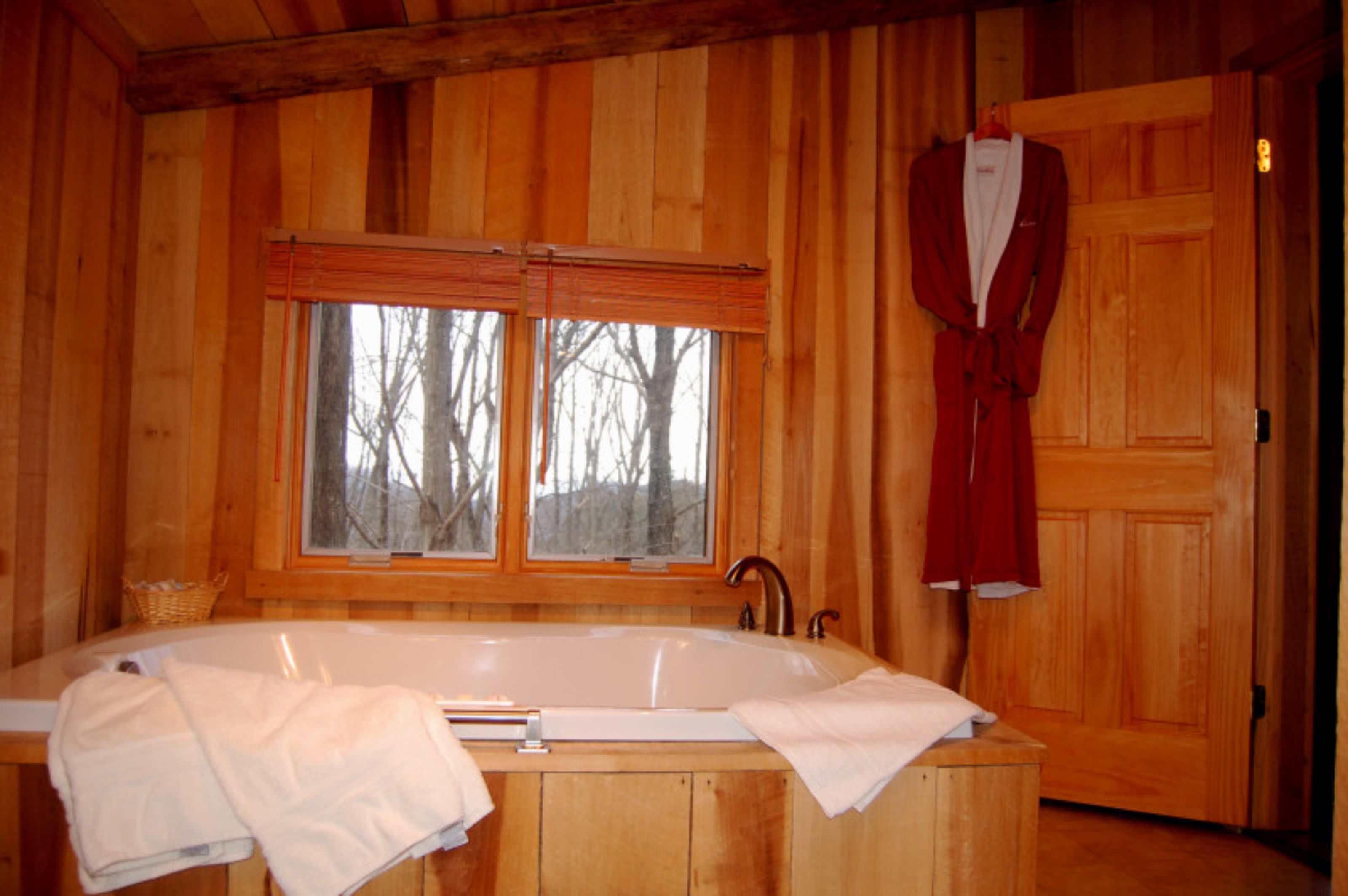 Una cabaña de madera con una bañera grande, dos ventanas y una bata colgada en la puerta.