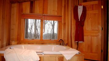 Una cabaña de madera con una bañera grande, dos ventanas y una bata colgada en la puerta.