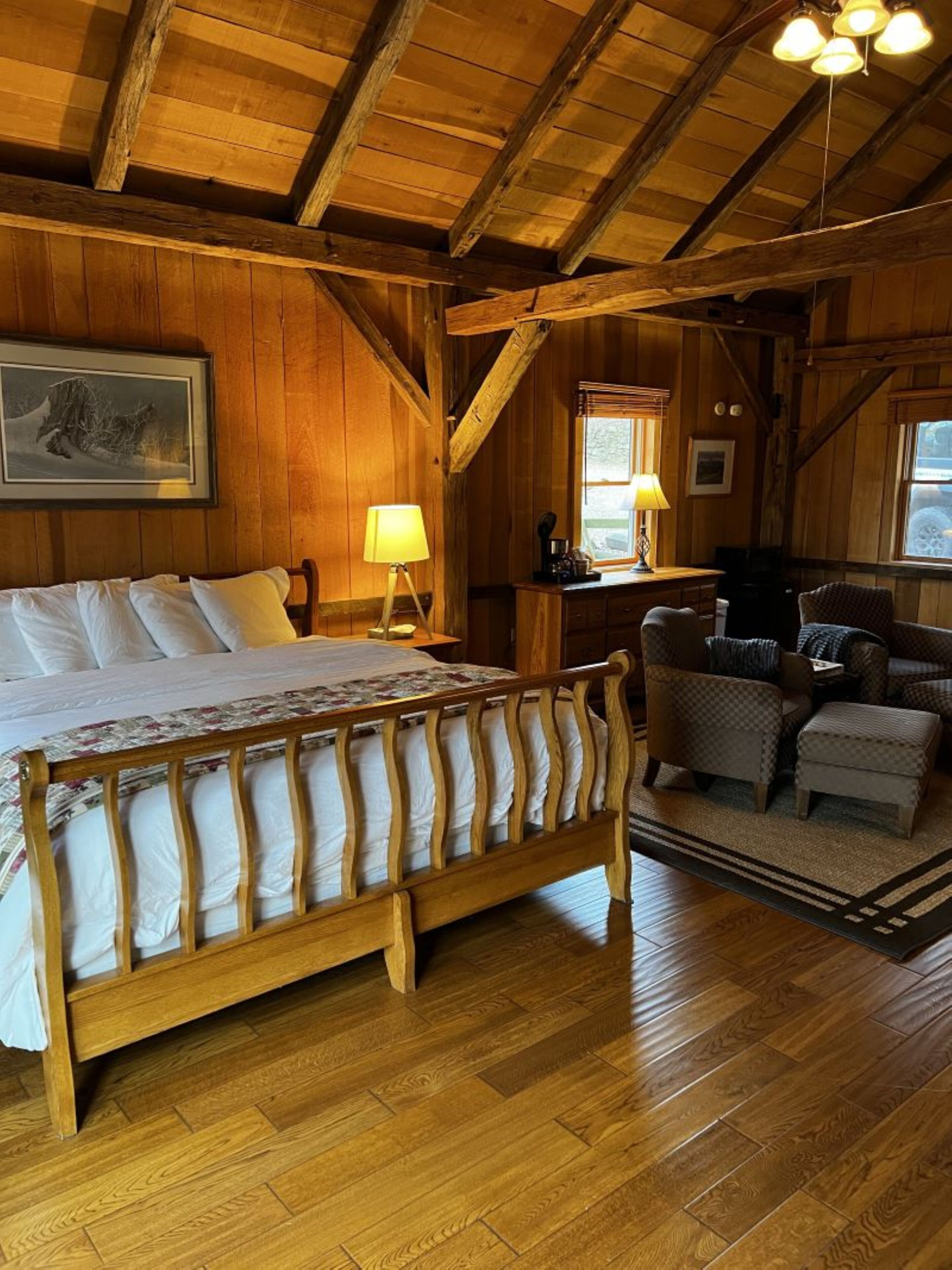Een houten slaapkamer met een bed, twee lampen, een bureau en een stoel.
