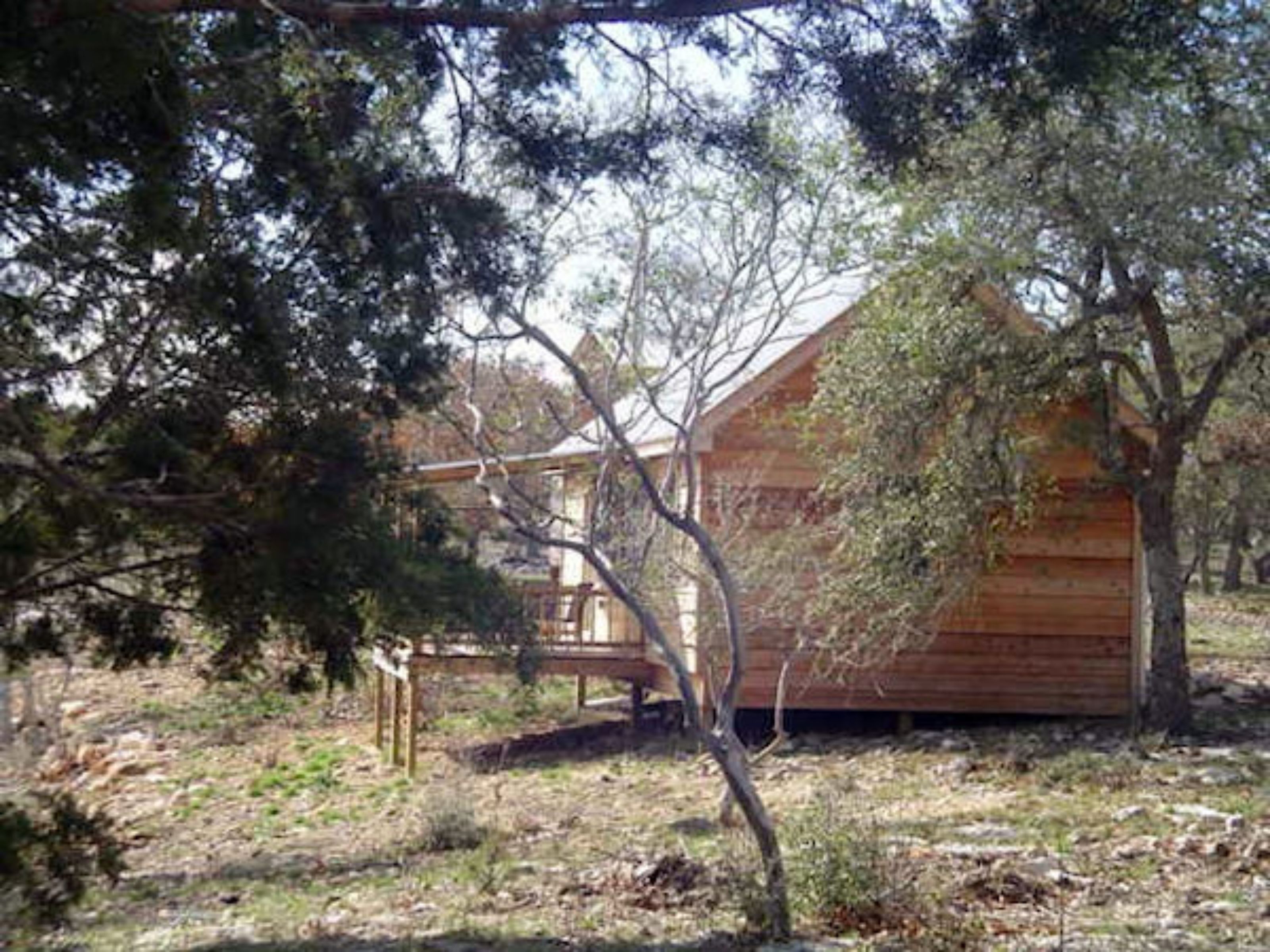 Una cabaña de madera con un porche, rodeada de árboles y un césped.