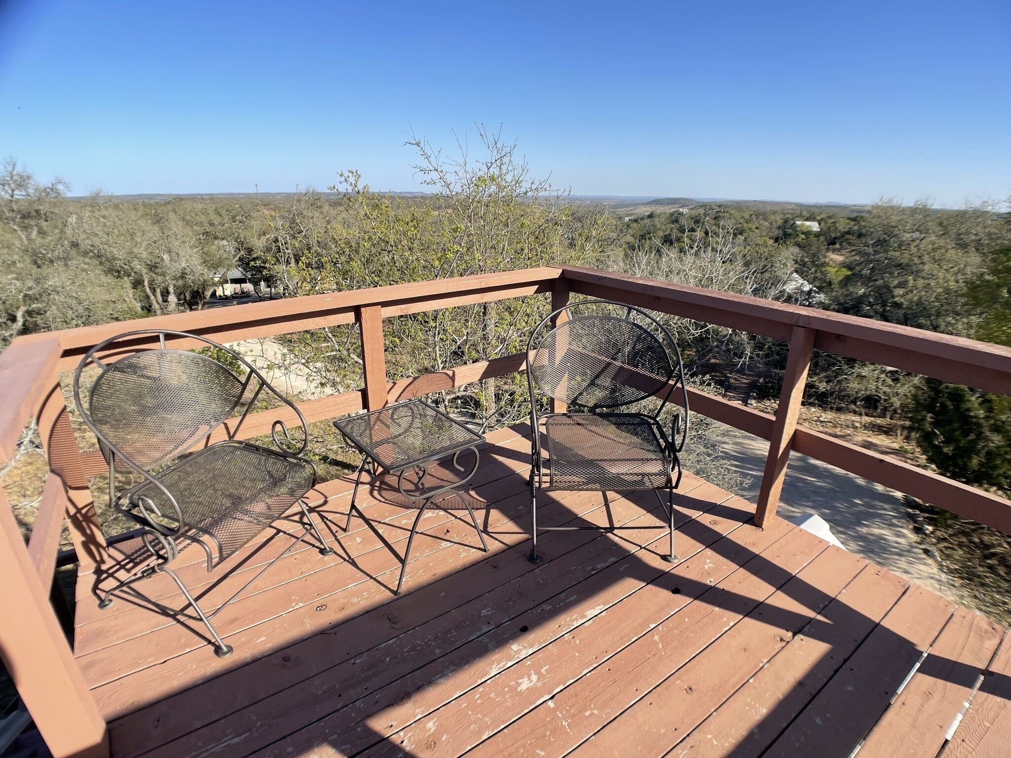 A wooden deck with metal chairs and a table, overlooking a dry landscape with sparse vegetation.