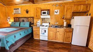 Une chambre confortable, aménagée dans le style d’un chalet, avec un lit, des armoires en bois, un poêle et un réfrigérateur.