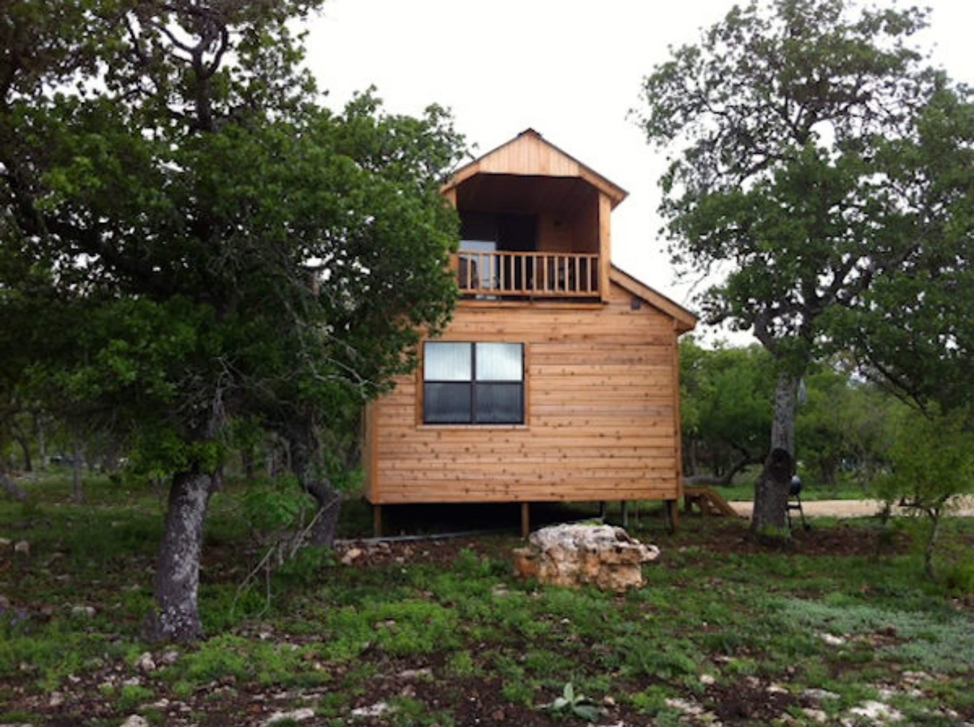 Una cabaña de madera con balcón, rodeada de árboles.