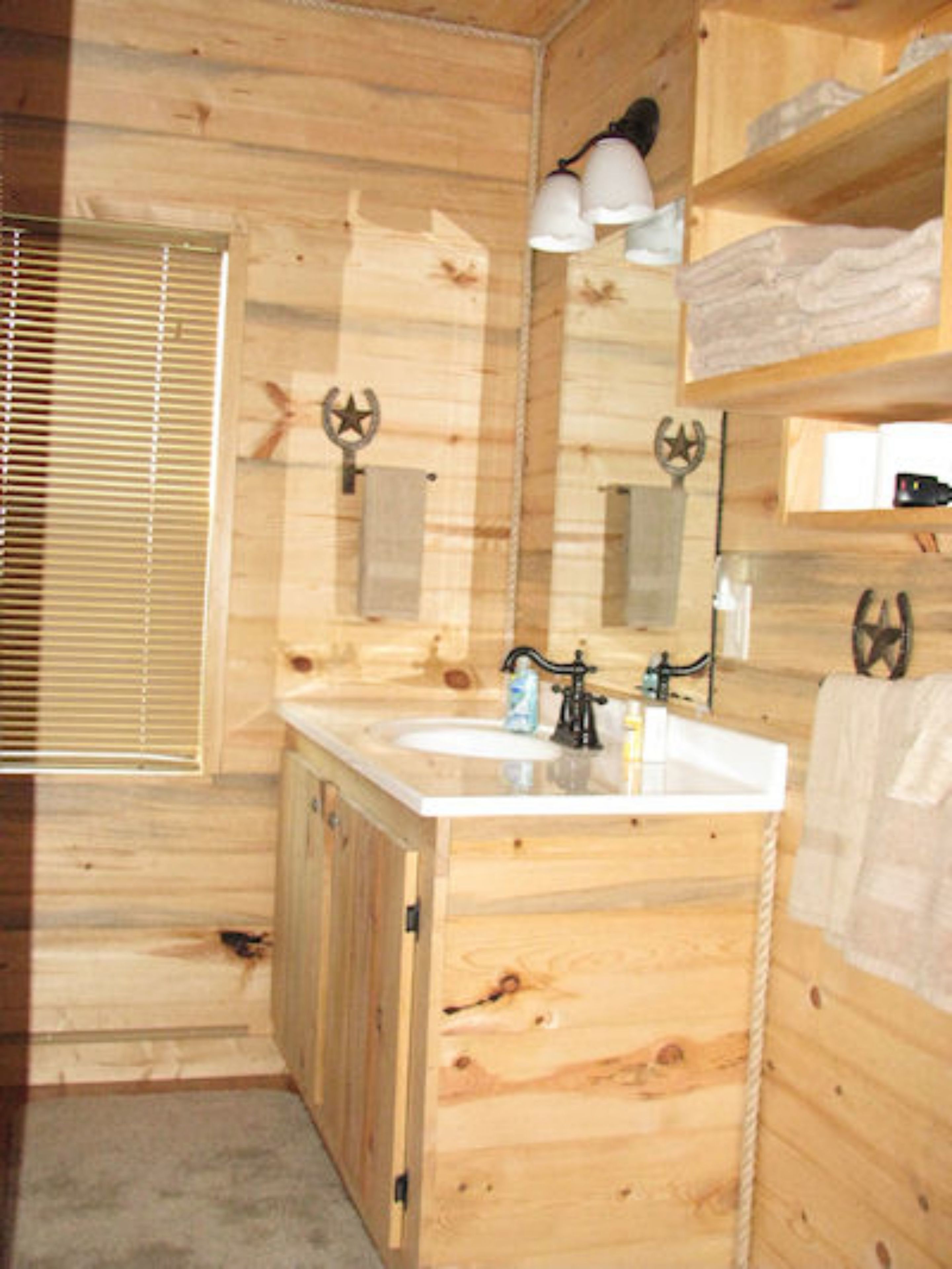 Baño de cabaña de madera con lavamanos doble, armarios de madera, un espejo y un perchero.