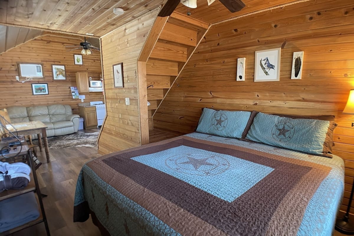 A cozy attic bedroom with a large bed, a wooden ceiling, and a small kitchenette.
