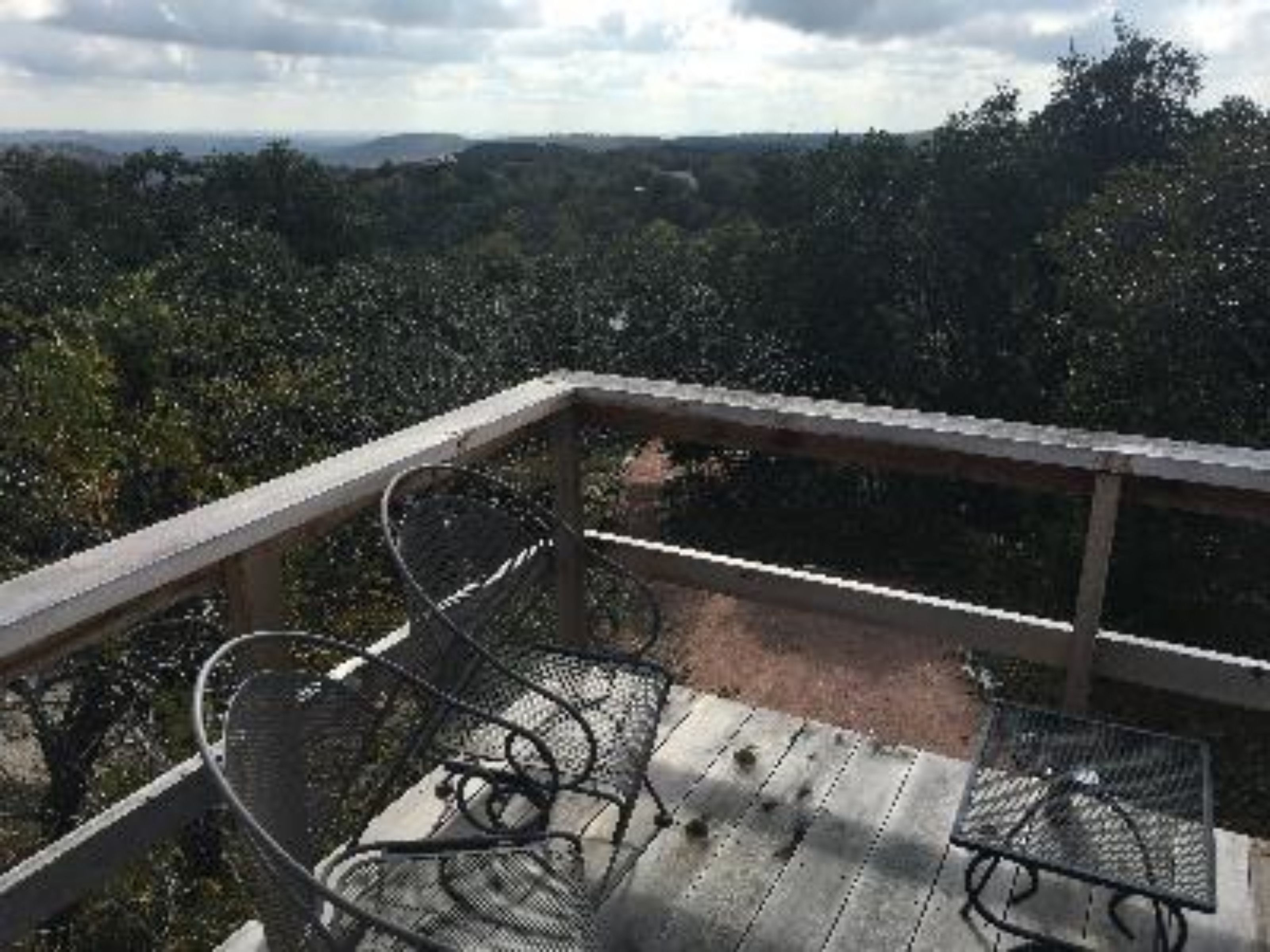 A wooden deck with metal chairs and a table, overlooking a forested landscape.