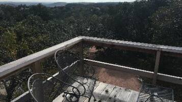 A wooden deck with metal chairs and a table, overlooking a forested landscape.