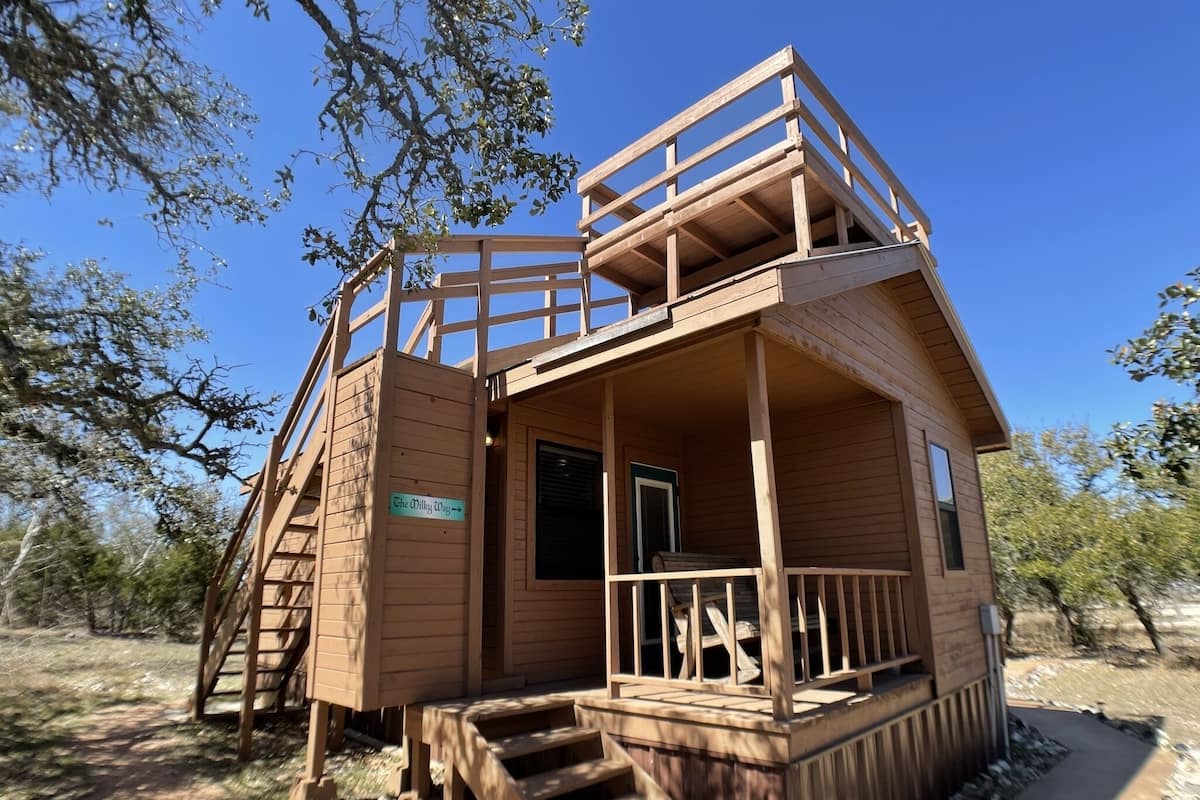A wooden cabin with a balcony, a staircase, and a sign indicating 'The Wilky Way'.