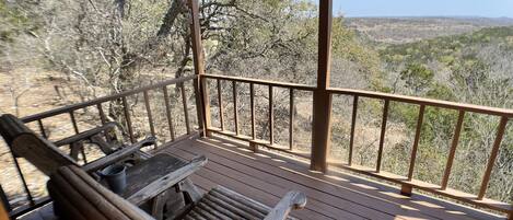 A wooden deck with a bench and a table, overlooking a hilly landscape.