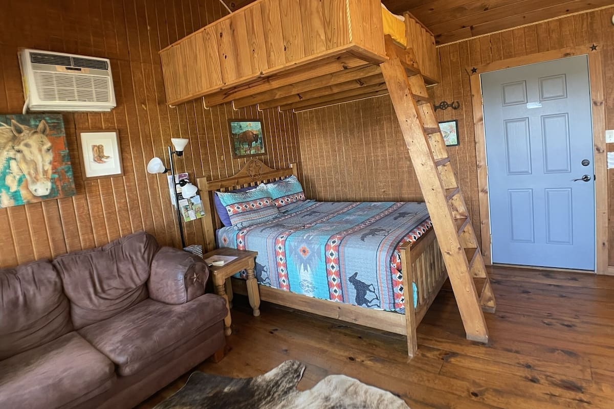 A wooden cabin room with a bunk bed, a leather sofa, a lamp, and a door.