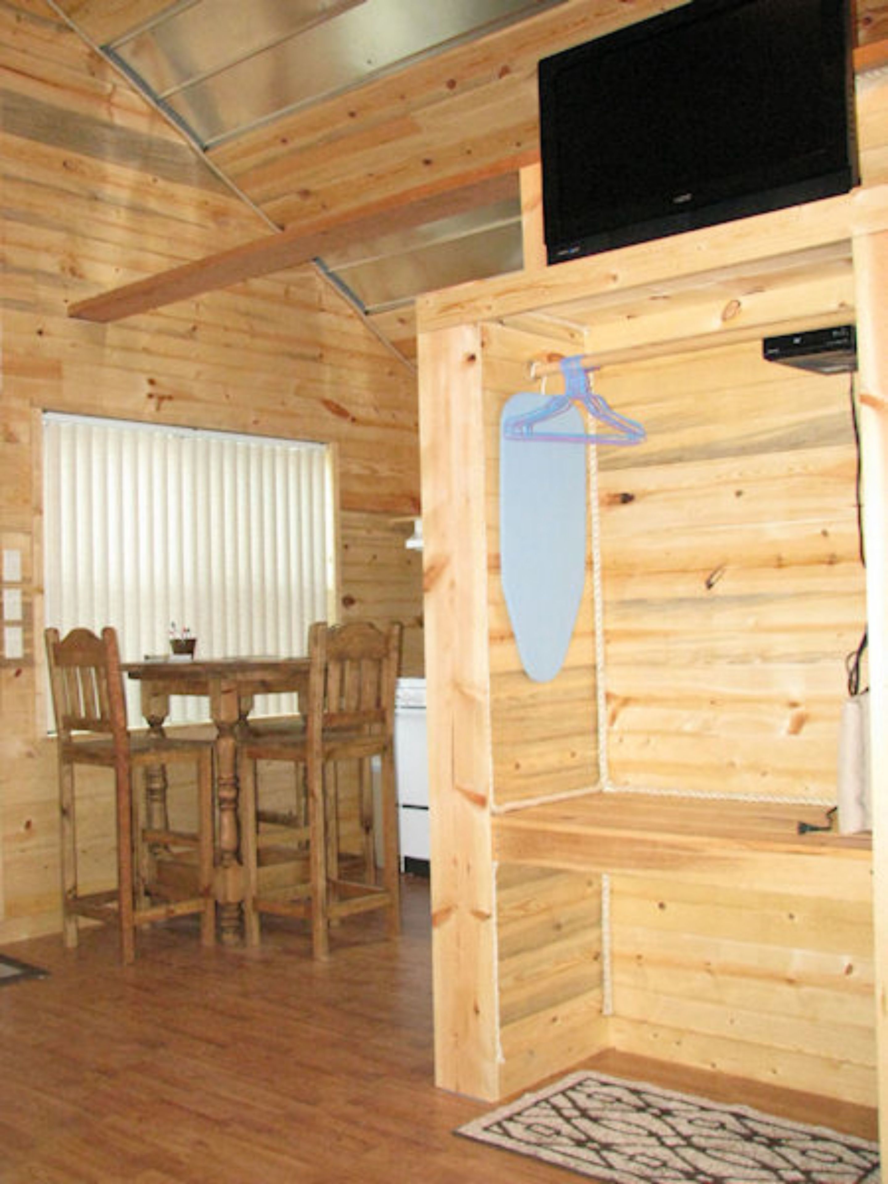 Un interior de madera con una mesa de comedor y sillas, un televisor montado en la pared y un perchero colgado.