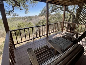 A wooden deck with a railing, benches, and a view of a dry, hilly landscape with sparse vegetation. - Walnut Canyon Cabins (Fredericksburg)