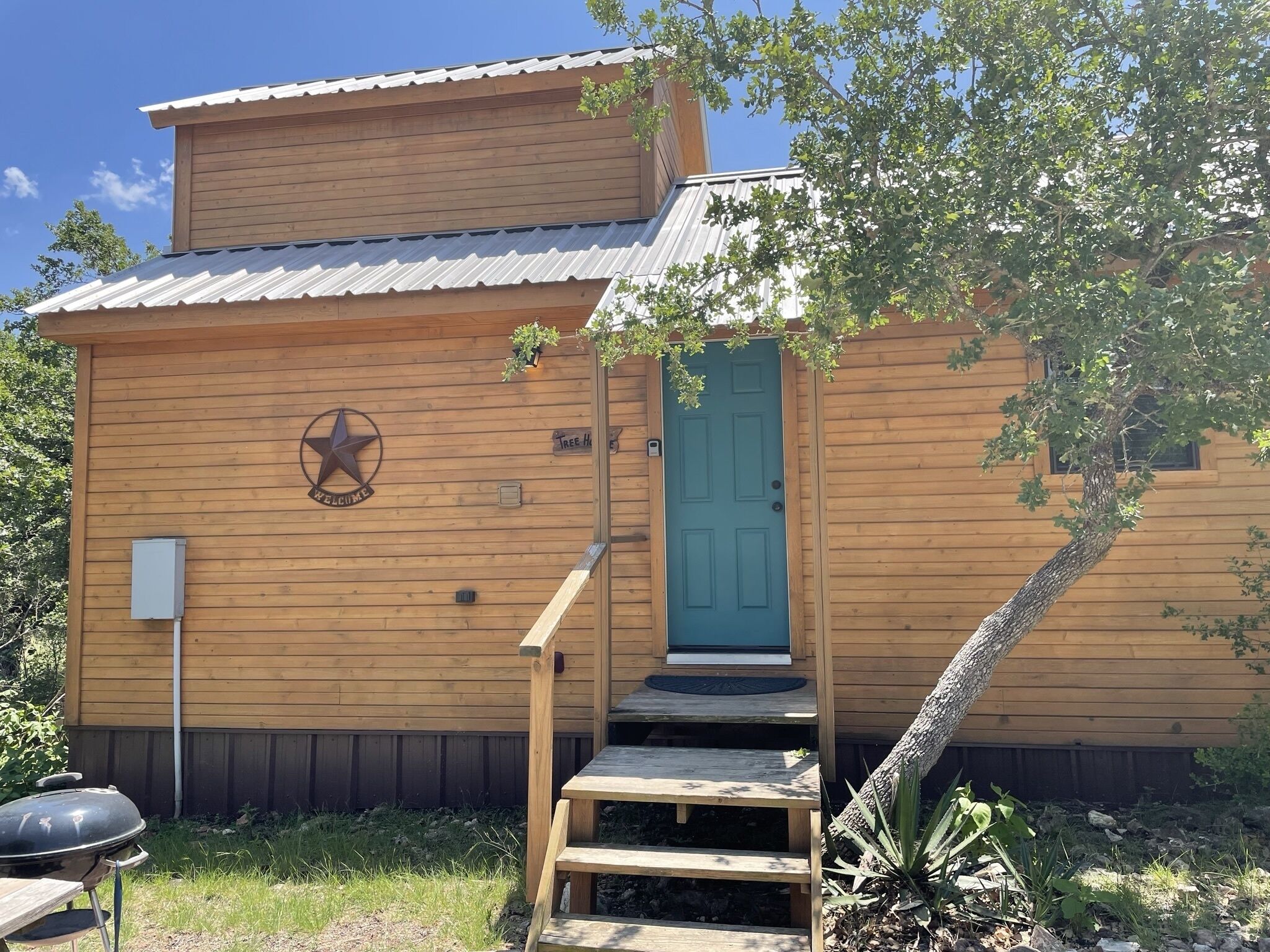 A wooden cabin with a blue door, a welcome sign, and a star logo.
